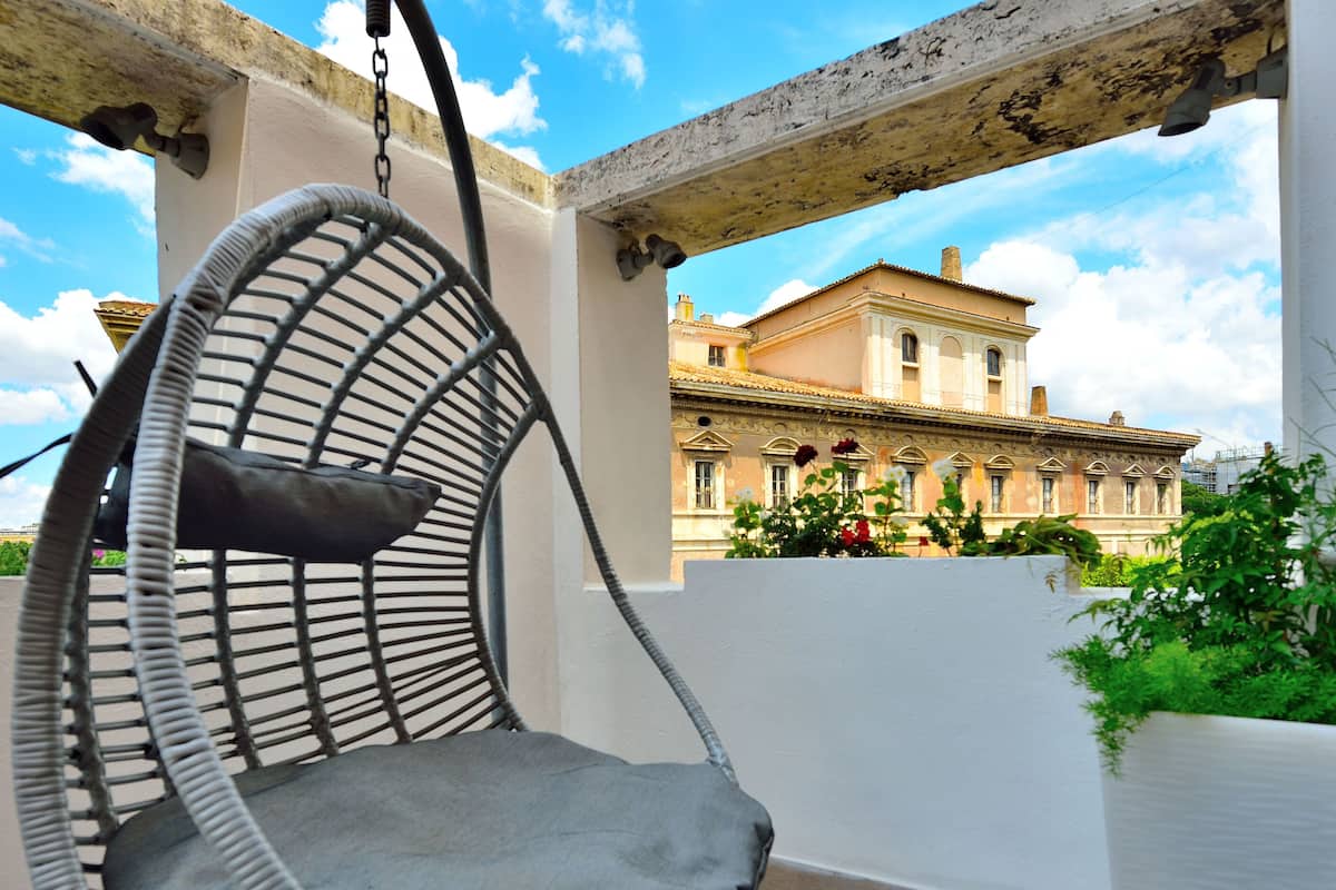 A wicker chair with a cushion in a covered outdoor area with a view of a historic building.