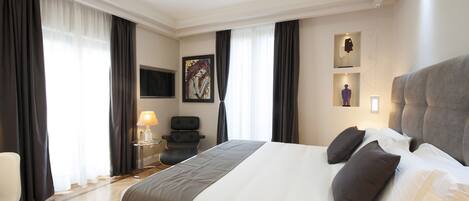 A hotel room with a large bed, a desk, a chair, and a TV on the wall.