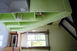 A room with a green accent wall, a window with curtains, and a small shelf with items.