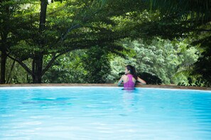Una mujer con traje de baño morado sentada en una piscina rodeada de exuberante follaje.