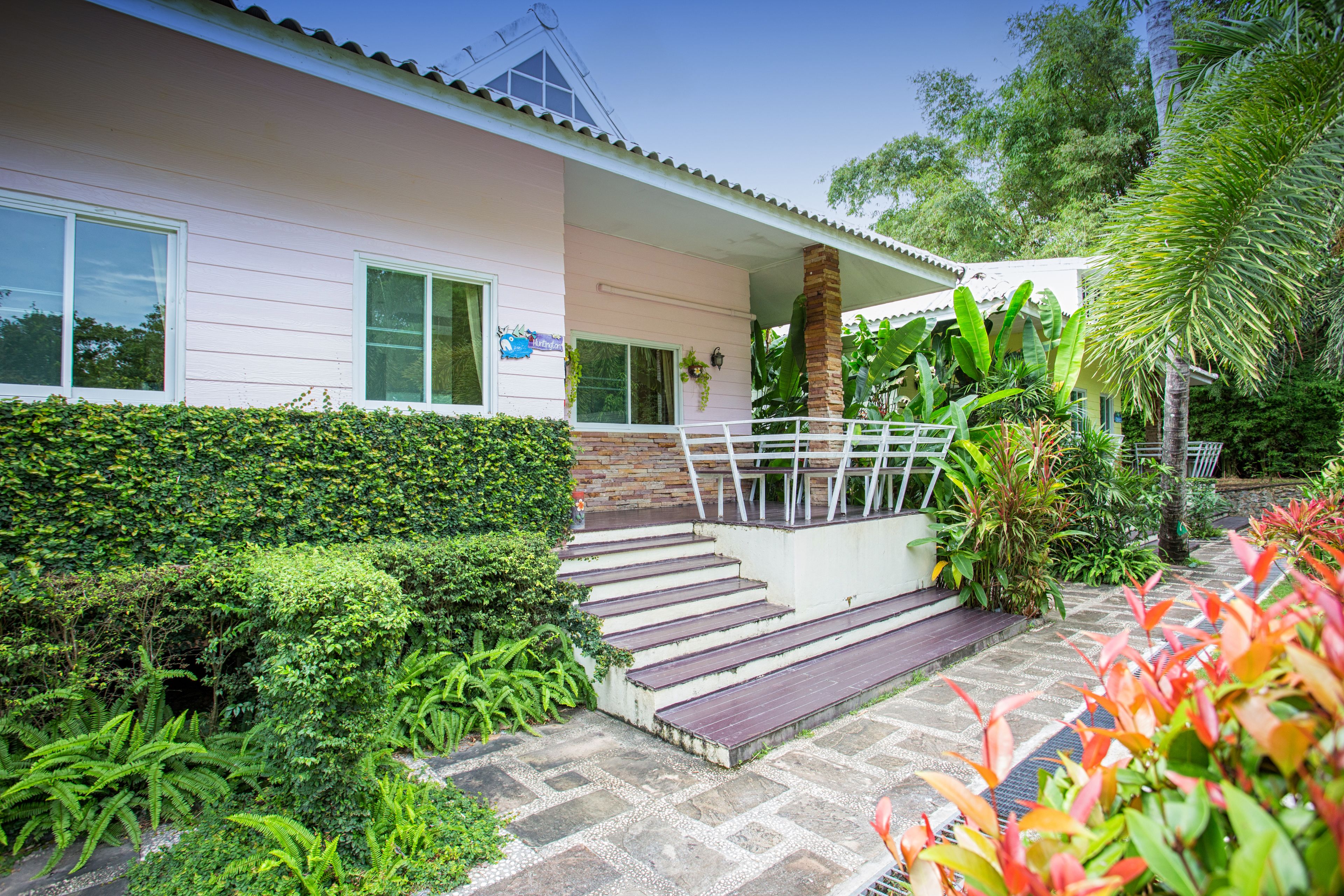 Ein zweistöckiges Haus mit einer Veranda, Treppen und einem Garten mit verschiedenen Pflanzen.