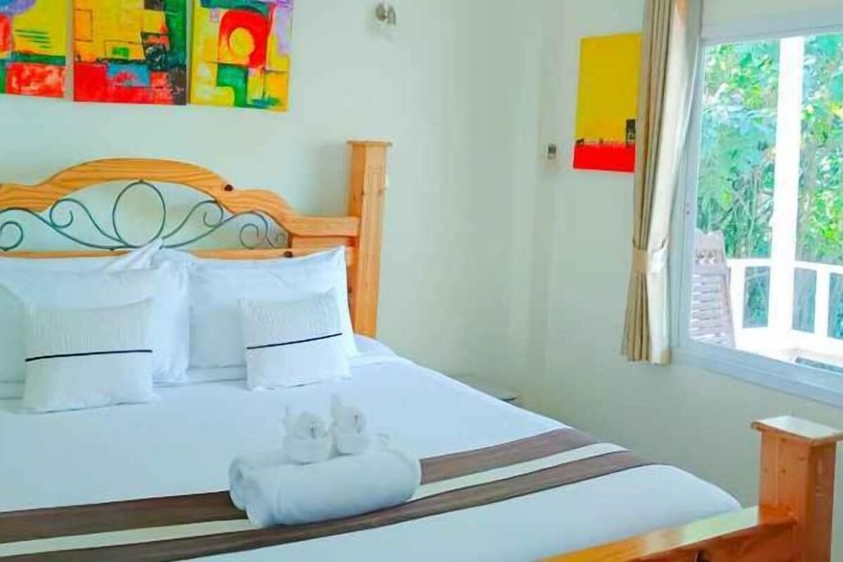 Una cama con ropa blanca y almohadas, un cabecero de madera y una ventana con cortinas.