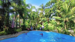 Une piscine entourée d’une végétation luxuriante et de palmiers, où l’on peut voir des gens nager et se détendre.