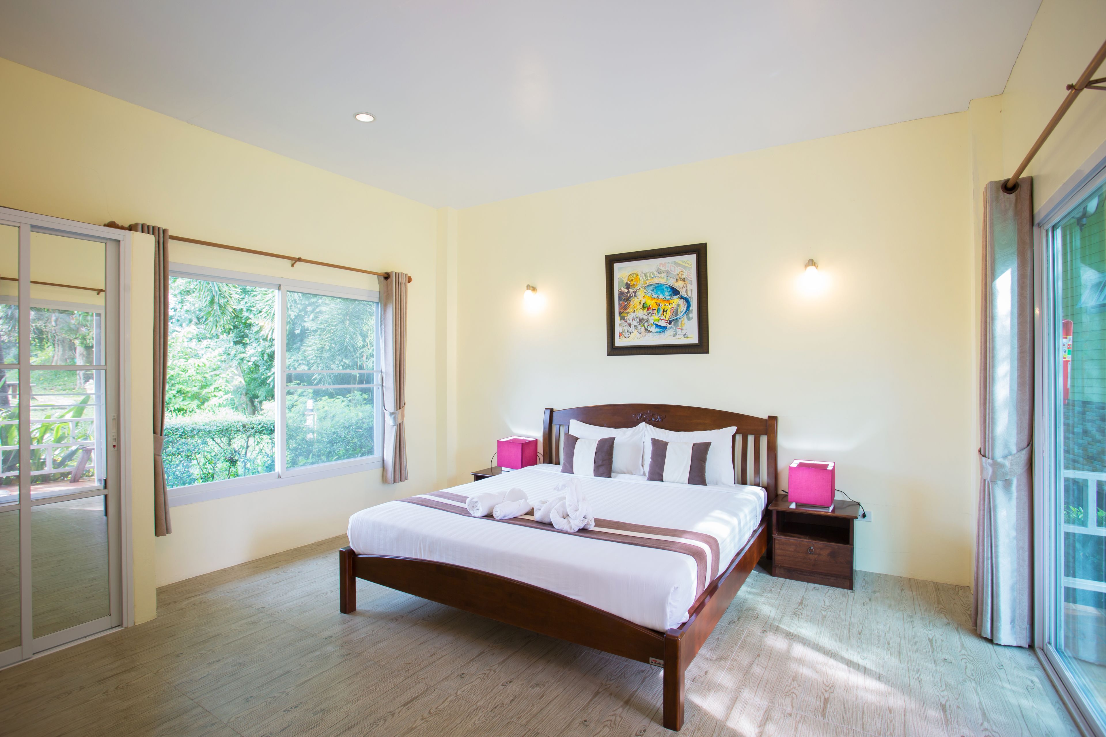 A bedroom with a large bed, a nightstand, a window with curtains, and a painting on the wall.