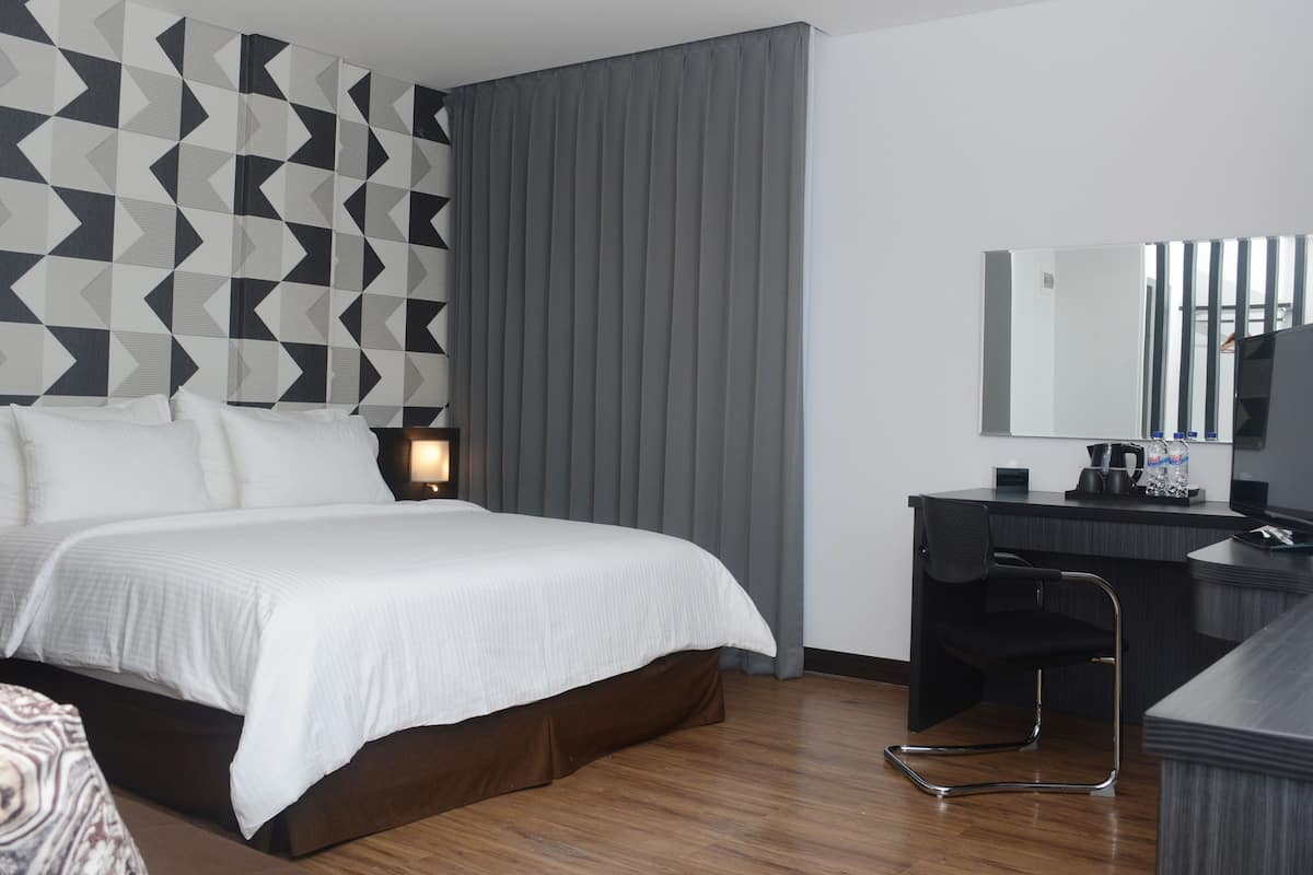 A modern hotel room with a large bed, a desk, and a mirror.