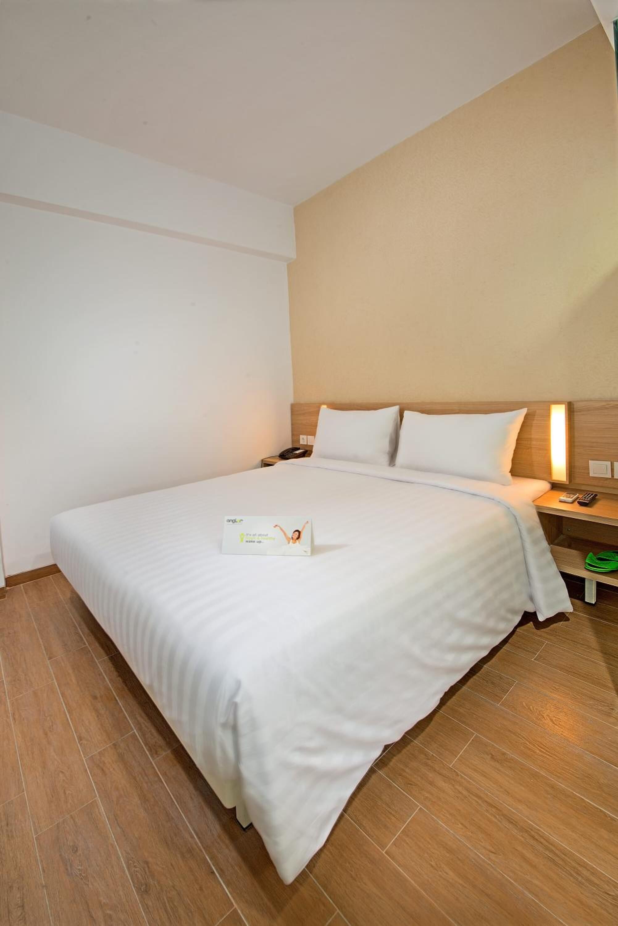Et hotelværelse med en stor seng, et sengebord med en lampe og et grønt skoskab.