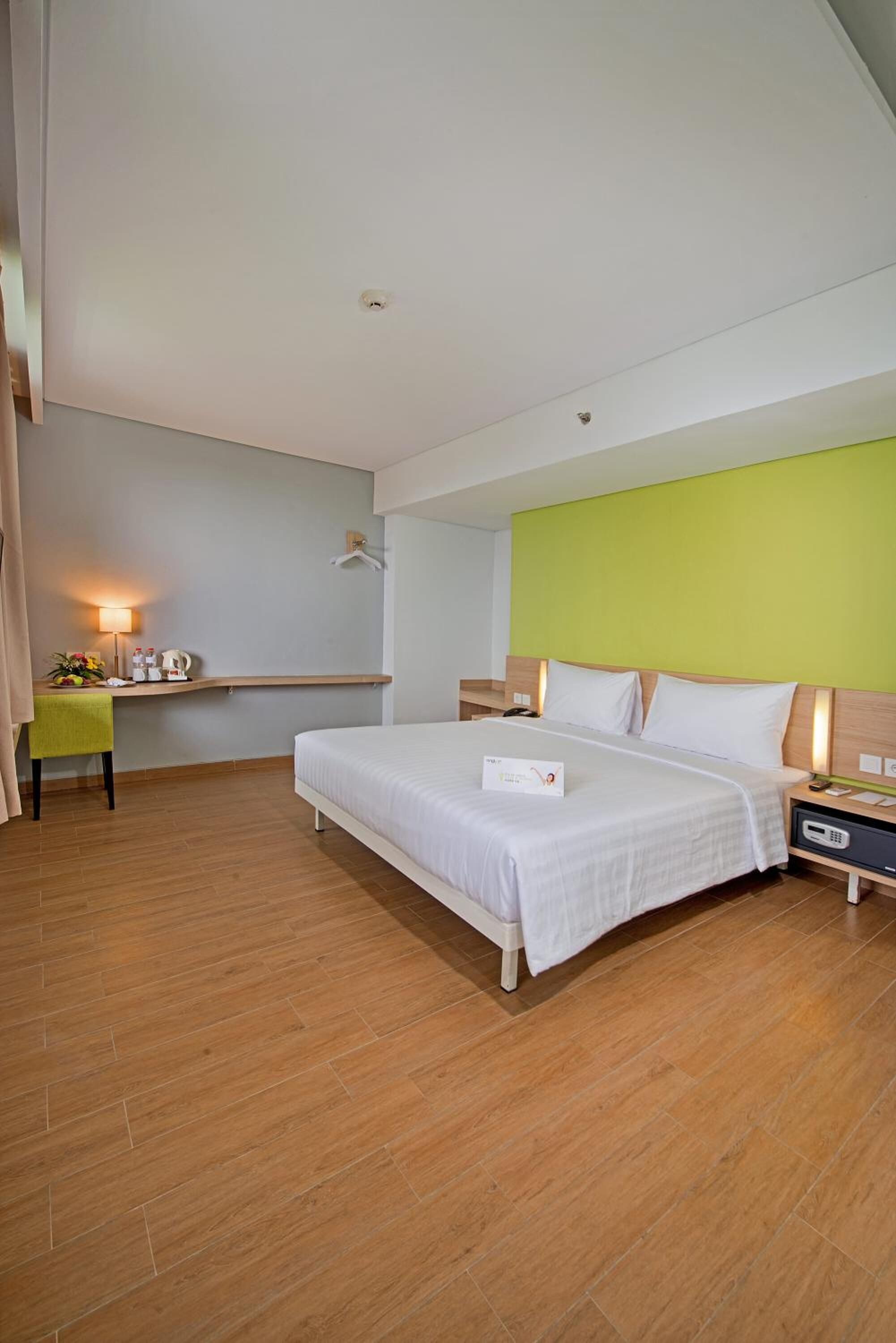 A hotel room with a bed, bedside table, lamp, and a small desk with a chair.