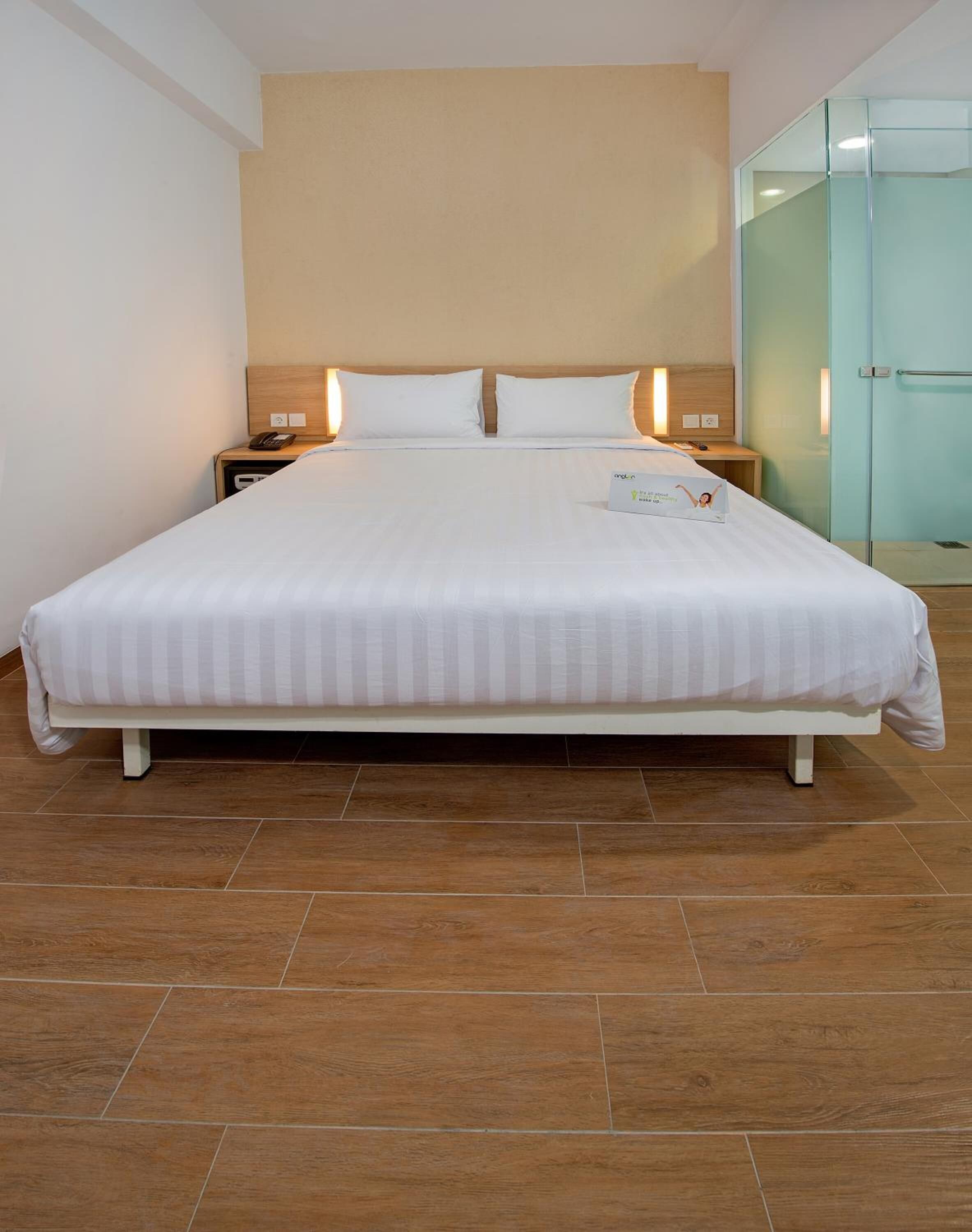 Habitación de hotel con una cama grande, piso de madera y un armario de vidrio.