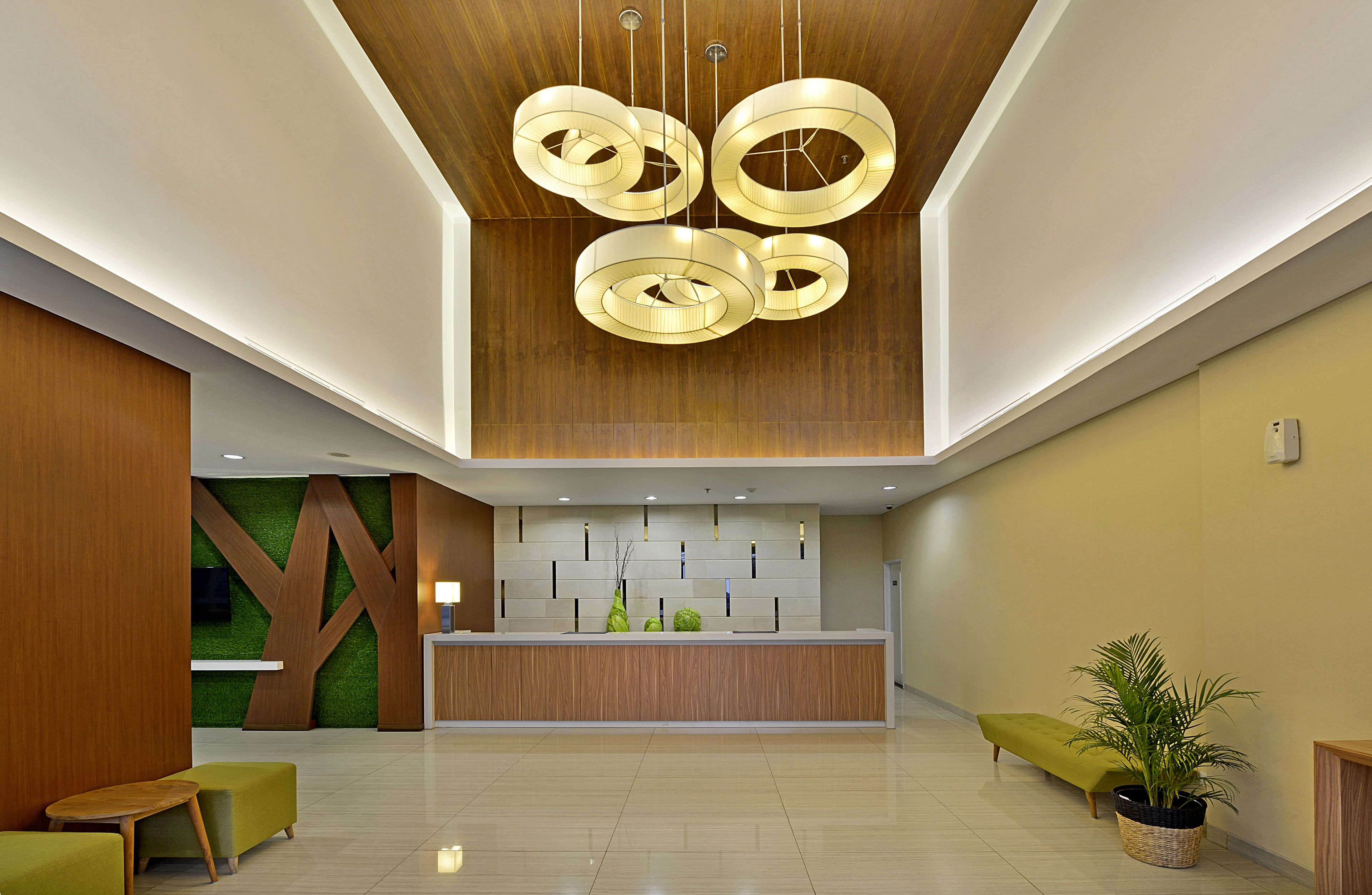 A modern reception area with a wooden reception desk, green seating, and a ceiling with circular light fixtures.
