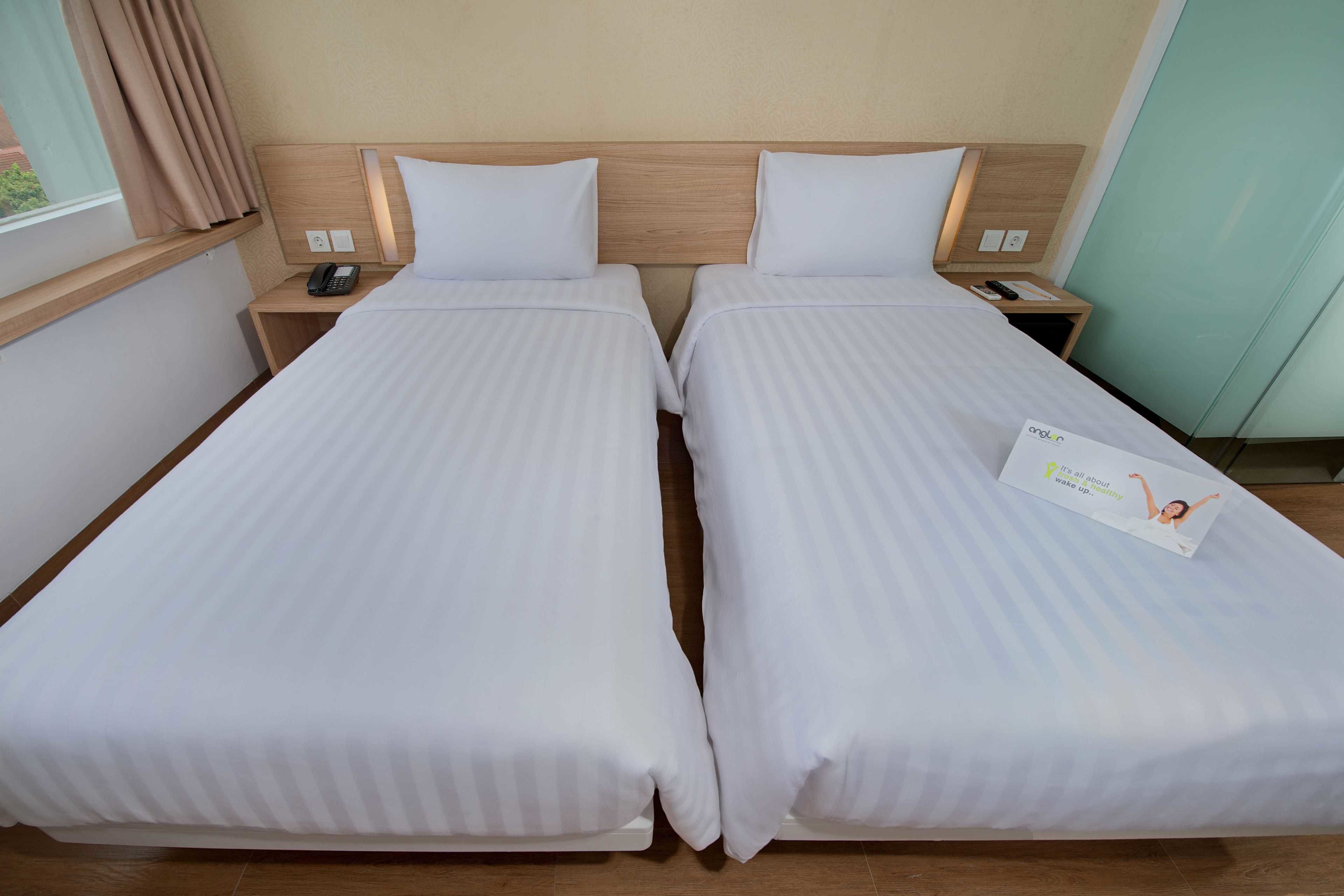 Quarto de hotel com duas camas de solteiro, cabeceiras de madeira, mesas de cabeceira com abajures e uma janela com cortinas.