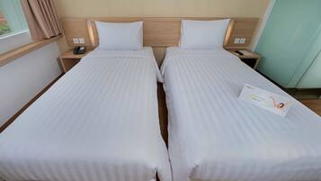 Quarto de hotel com duas camas de solteiro, cabeceiras de madeira, mesas de cabeceira com abajures e uma janela com cortinas.