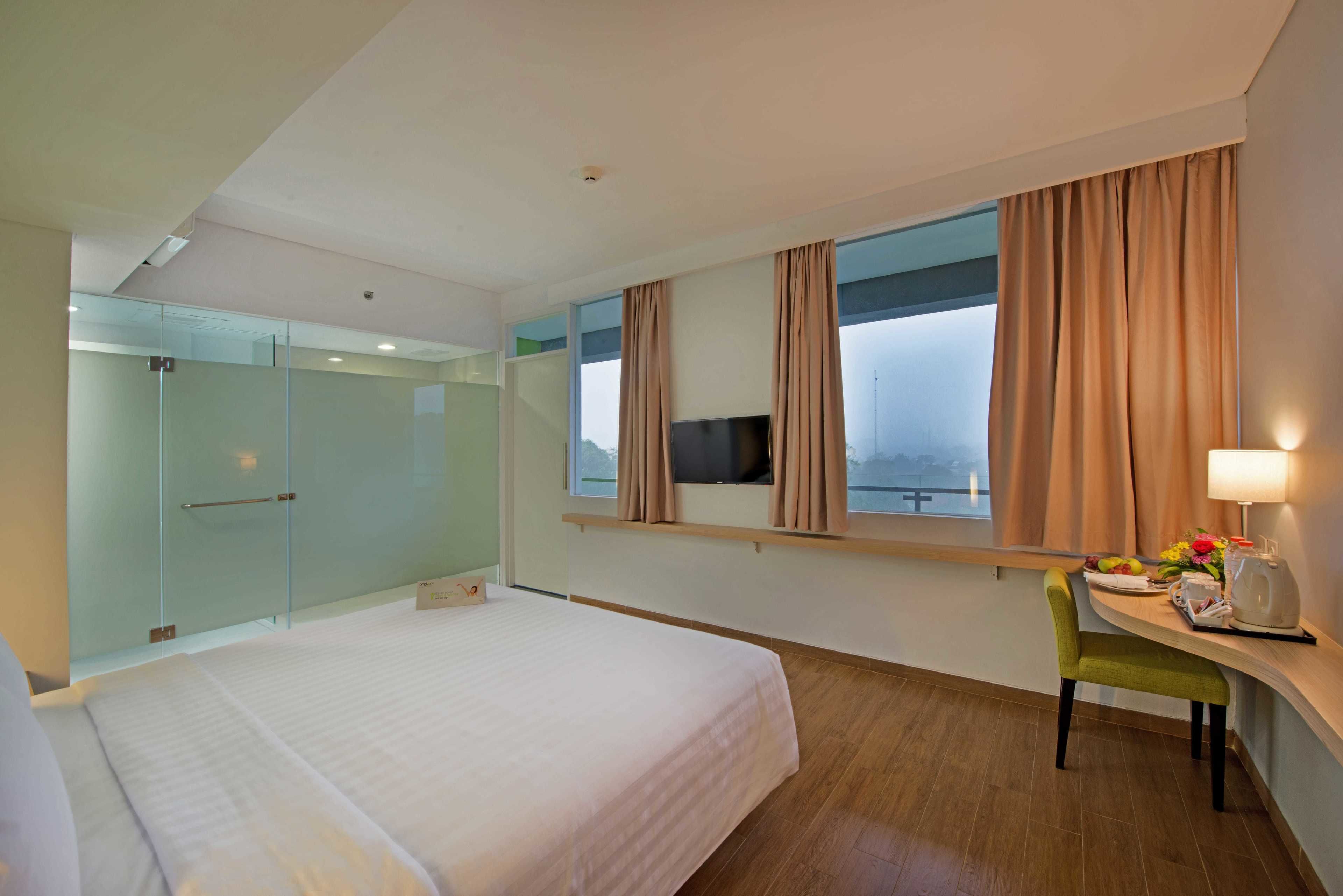 A hotel room with a bed, a desk with a lamp, a chair, a TV, and a window with curtains.