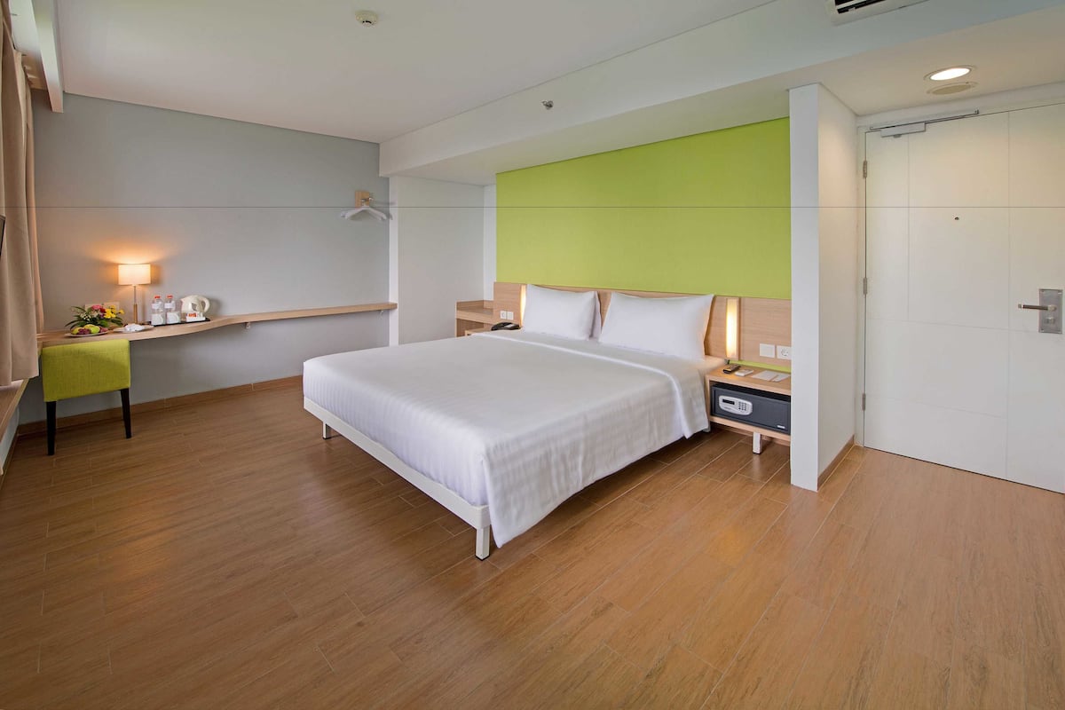 Una camera d'albergo moderna con un letto grande, comodini, una scrivania con una sedia e una parete verde a contrasto.