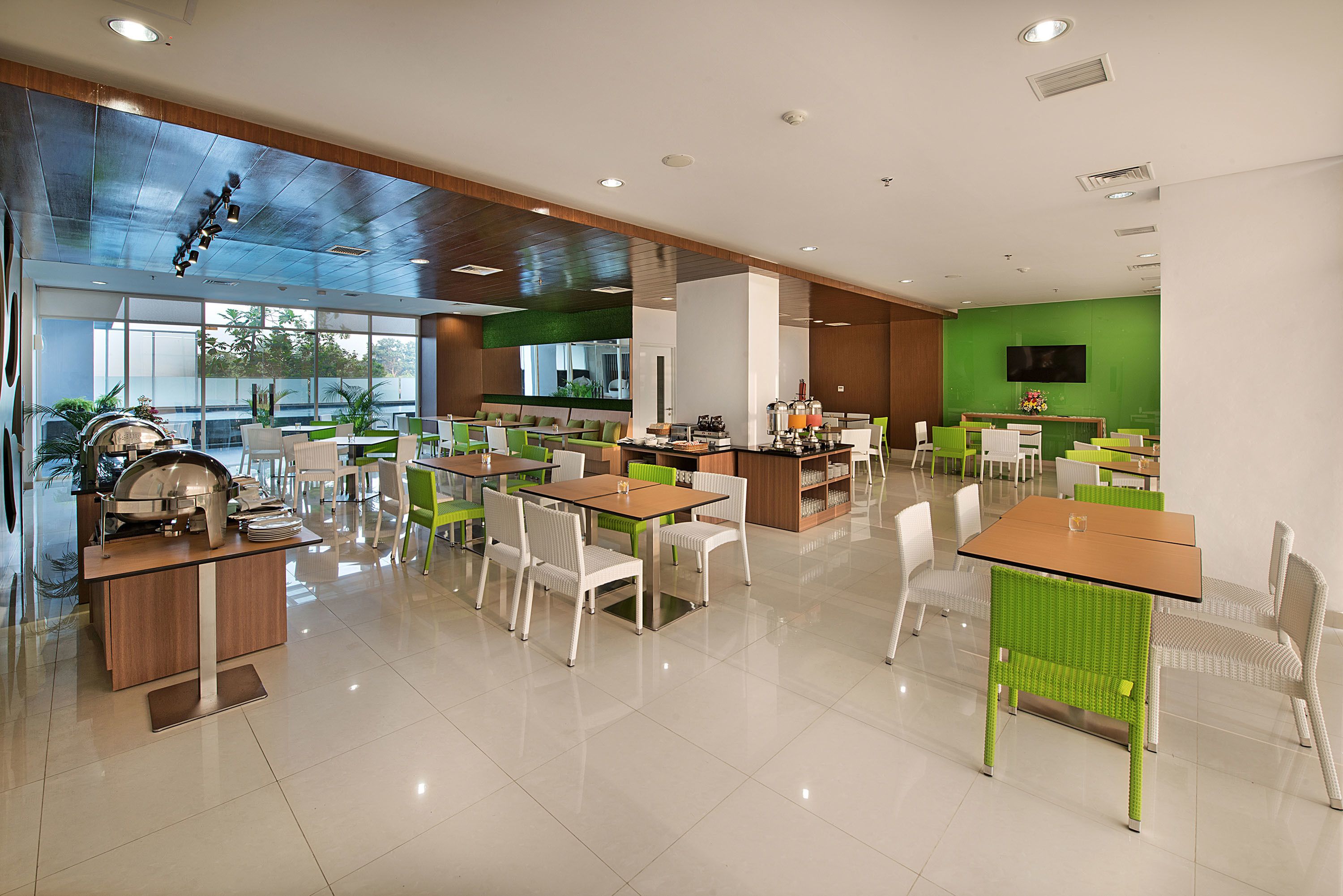 Un espace repas moderne, doté de plusieurs tables et chaises, d’un buffet et d’un mur d’accent de couleur verte.