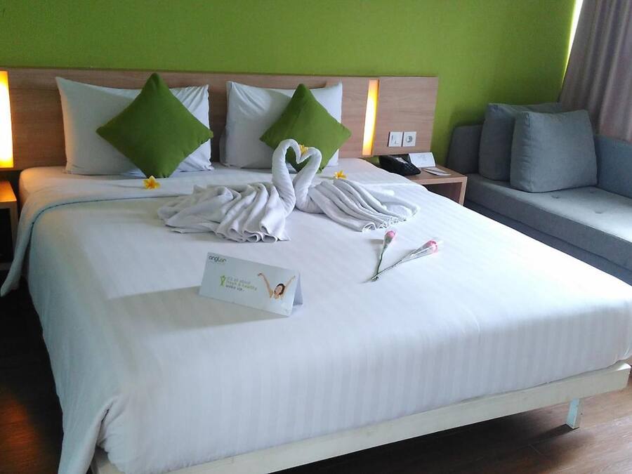 A hotel room with a large bed, a bedside table with a lamp, a sofa, and a green wall.