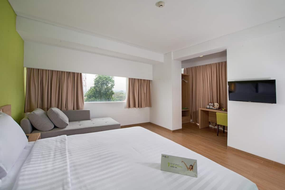 Camera d'albergo con un letto grande, una zona salotto con cuscini, una scrivania, una televisione e vista sull'esterno.