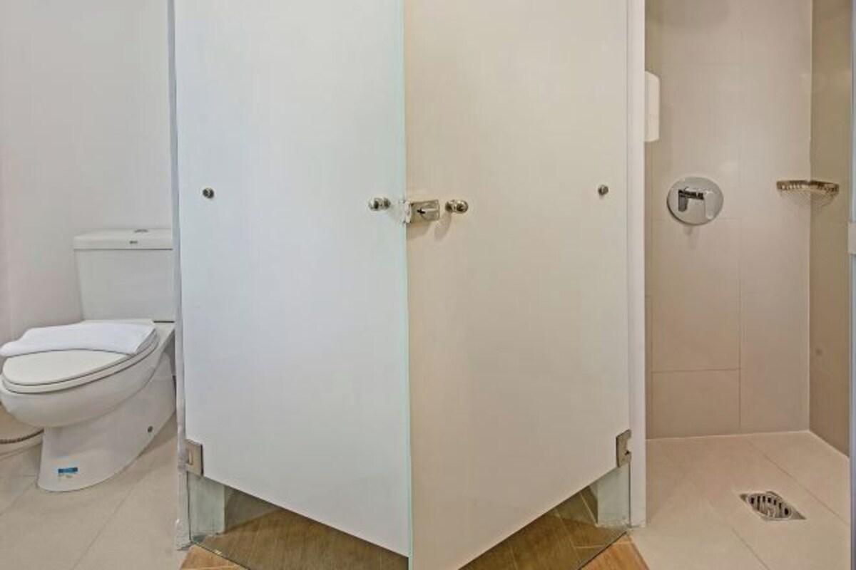 Une salle de bain avec des toilettes, un espace douche et une porte blanche avec une poignée argentée.