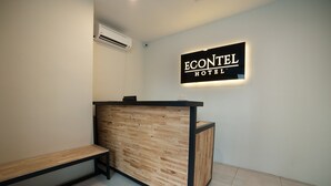 Balcão de recepção com acabamento em madeira e moldura preta, um banco à esquerda e uma placa acima com a inscrição 'ECONTEL HOTEL'.