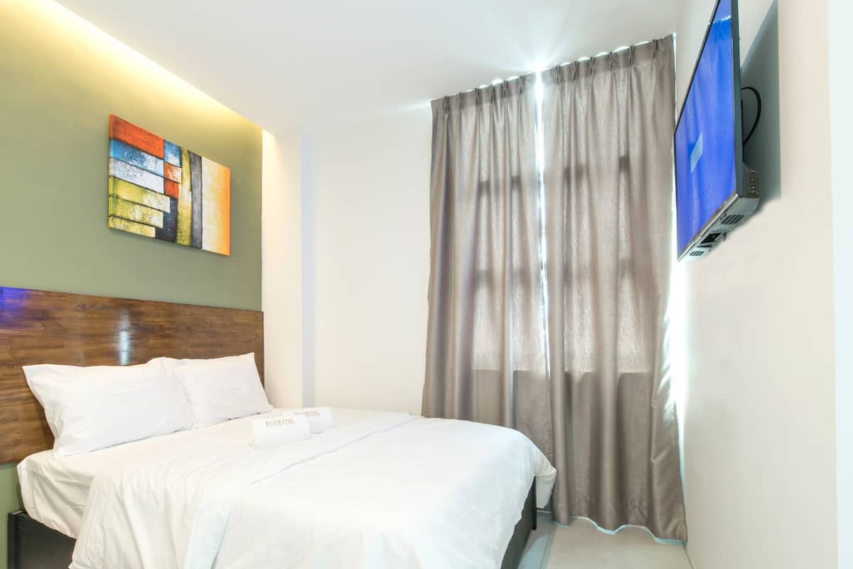 A hotel room with a bed, a television, a painting on the wall, and a window with curtains.