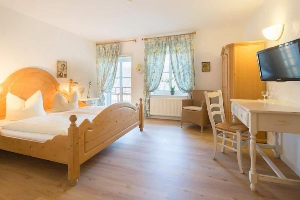 A bedroom with a wooden bed, a desk, a chair, and a television.