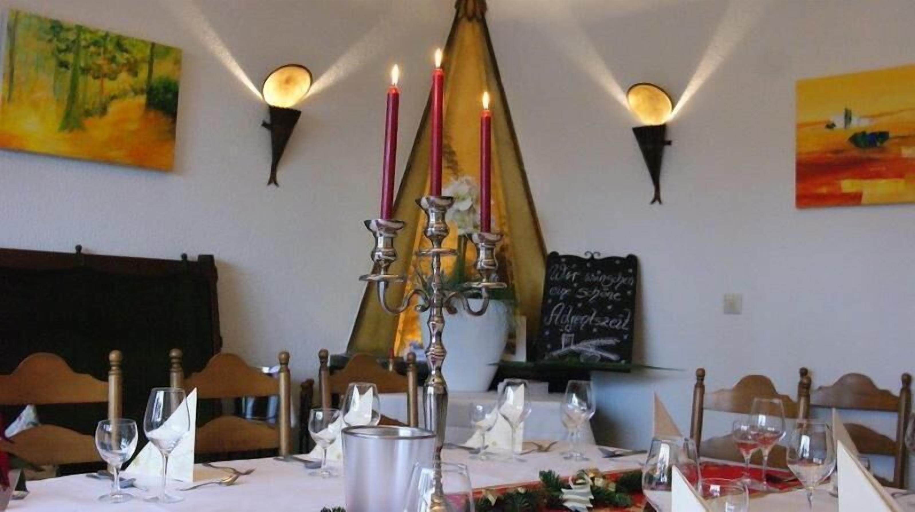 A dining area with a table set for two, candles, wall-mounted lights, and paintings.