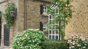 A brick building with a window and a door. There are bushes with pink flowers in front of the building. - Land-gut-Hotel Lohmann (Drensteinfurt)