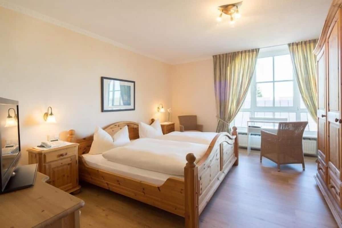 A hotel room with a wooden bed, bedside tables, a desk, and a chair.