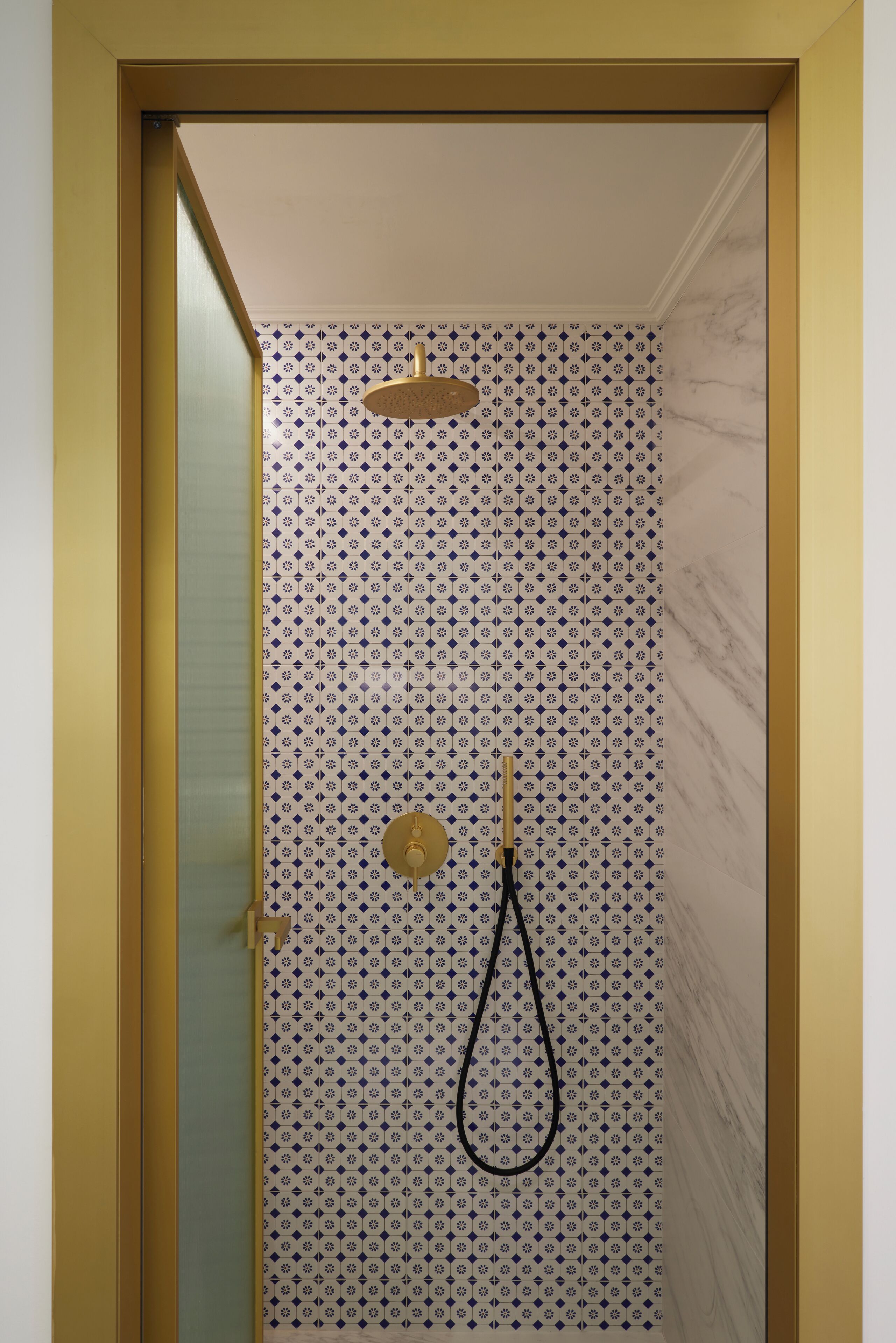 A shower with a patterned wall, a gold showerhead, and a black hose.