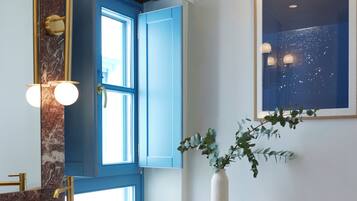 Une salle de bain avec un grand lavabo, des meubles bleus, un miroir avec éclairage intégré, une fenêtre et une chaise.
