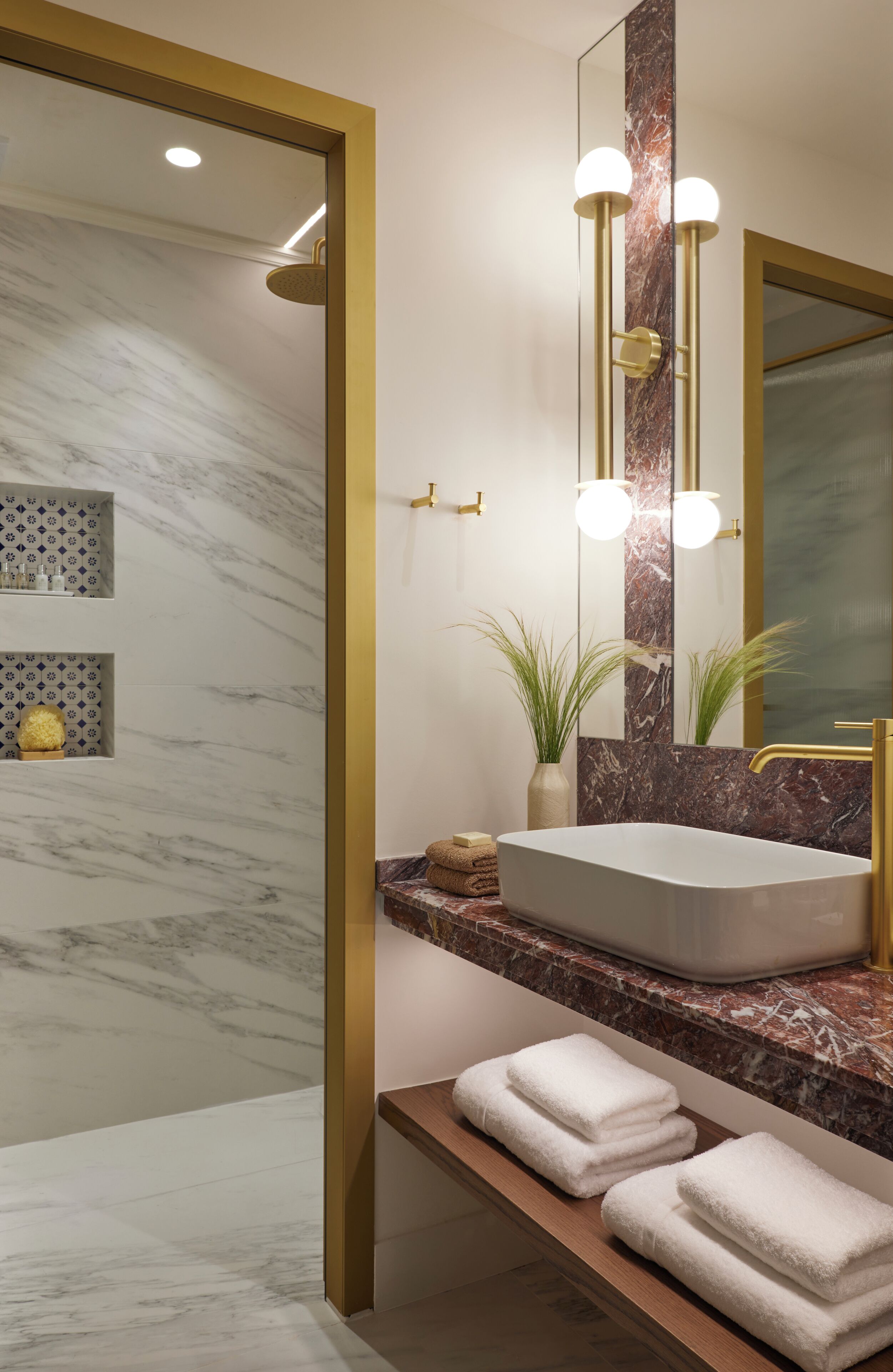 A modern bathroom with a marble wall, a large mirror, a gold-framed sink, and a shower area.