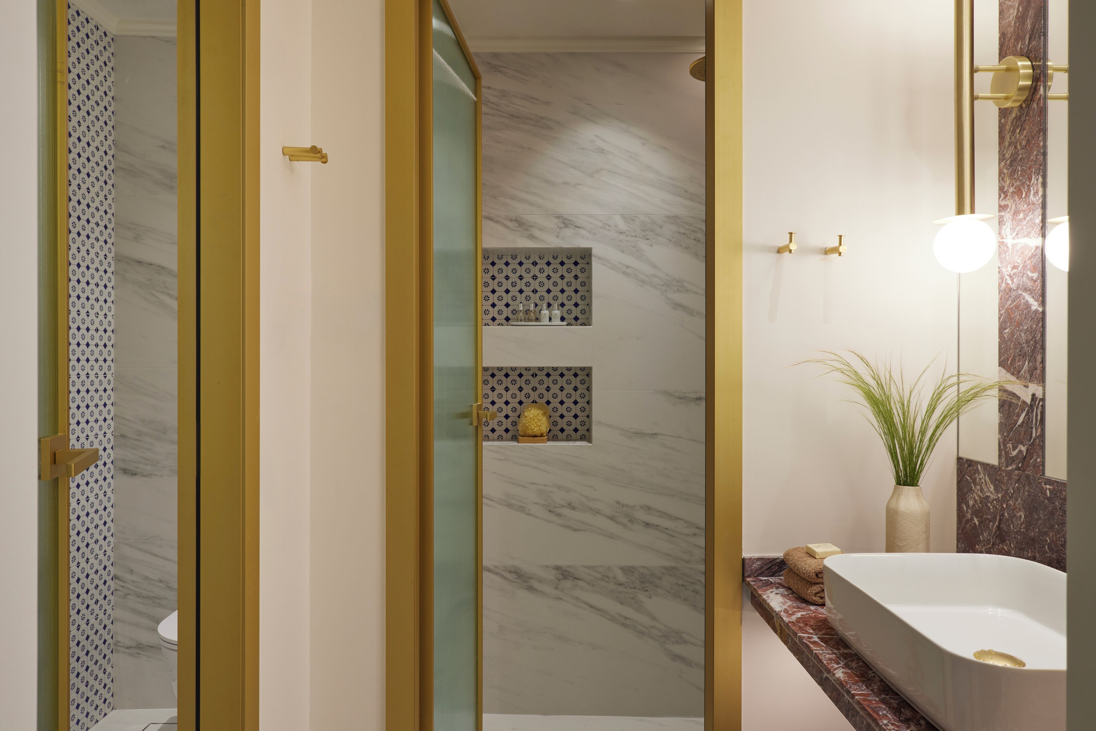 A modern bathroom with a marble shower, a built-in shelf with toiletries, and a large bathtub.