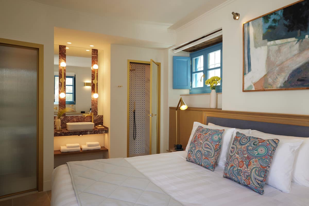 Habitación de hotel con una cama grande, un baño con espejo y tocador, y un cuadro en la pared.