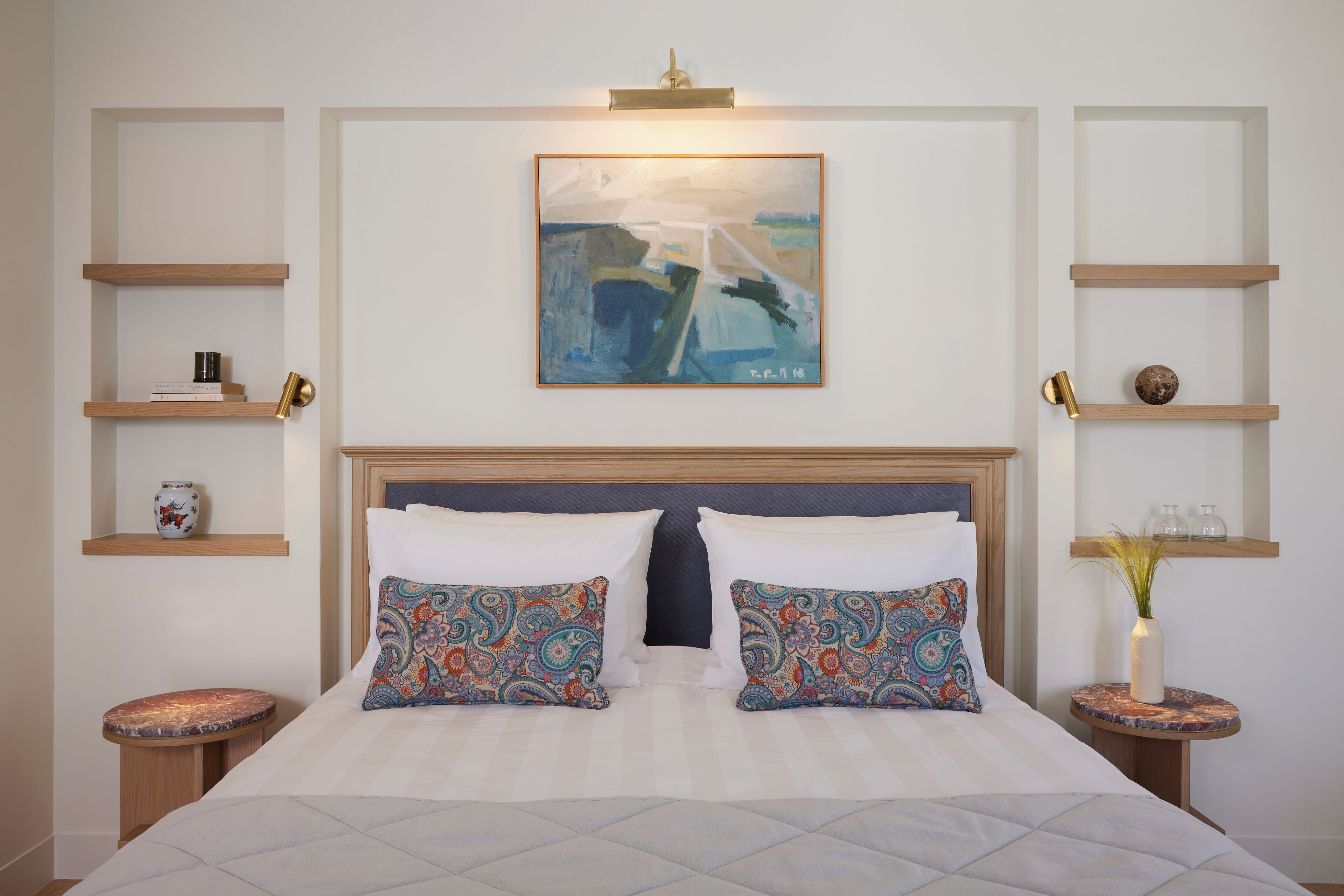 Ein ordentlich eingerichtetes Hotelzimmer mit einem großen Bett, zwei Nachttischen, einem Kopfteil und einem an der Wand hängenden Kunstwerk.