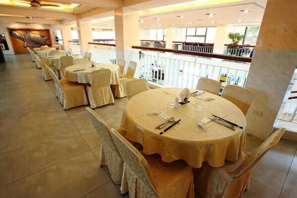 A restaurant with round tables covered in beige tablecloths, white chairs, and a balcony with a railing. - Art Spa Hotel (Jiaoxi)
