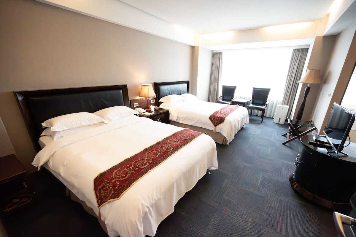 A hotel room with two beds, a desk, a chair, a television, and a window with curtains.