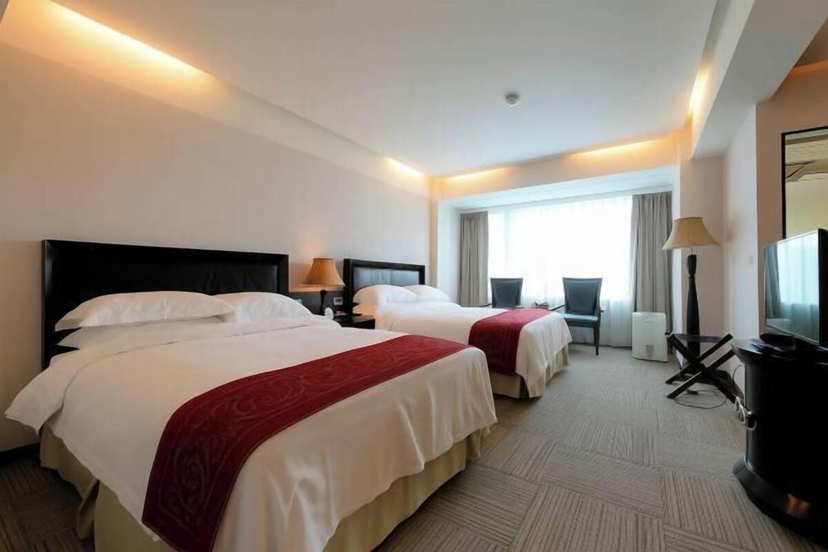 A hotel room with two beds, a TV, a heater, and a window with curtains.