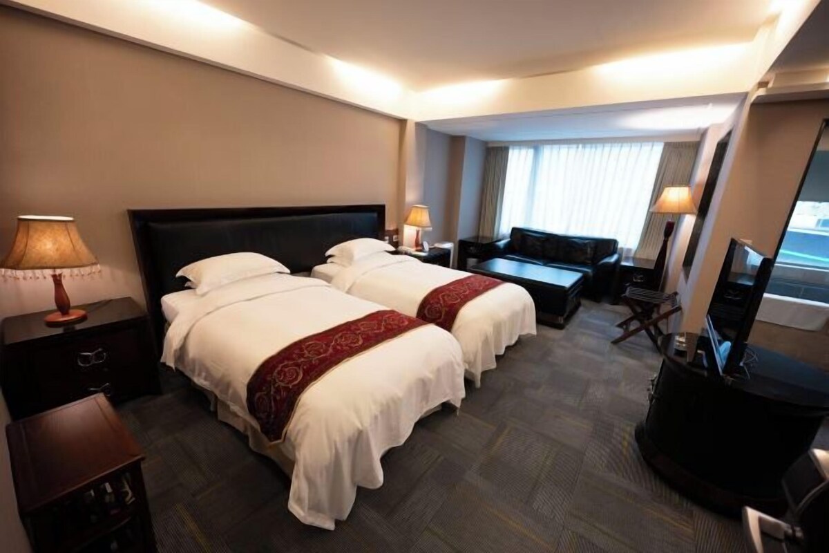 A hotel room with two beds, a desk, a chair, a television, and a window with curtains.