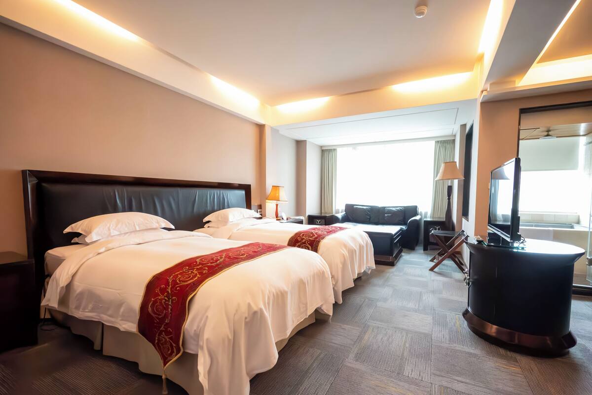 A hotel room with two beds, a sofa, a TV, and a large window.
