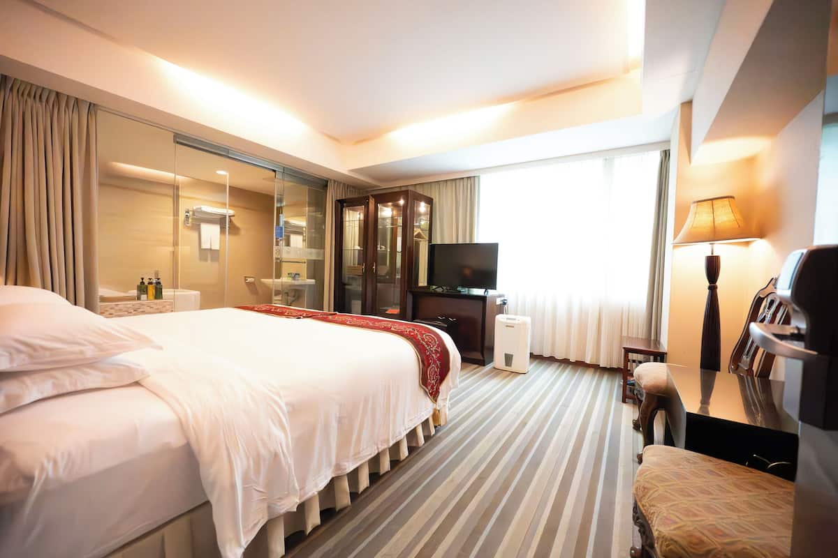 A hotel room with a large bed, a TV, a desk with a lamp, and a wardrobe.