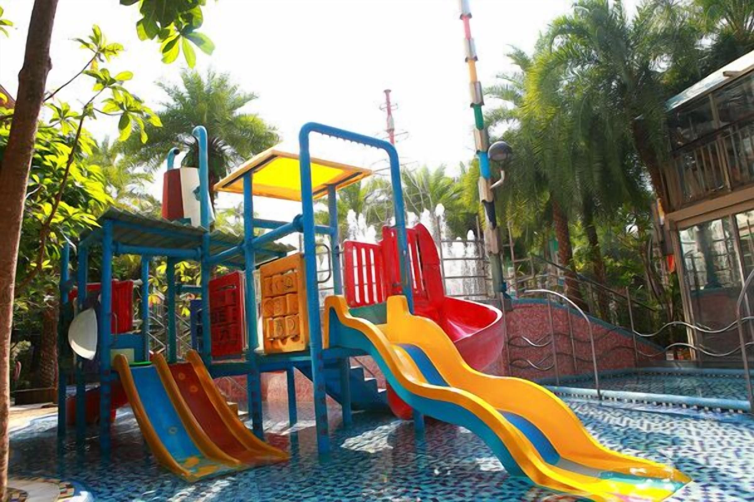 A playground with multiple slides and climbing structures surrounded by palm trees.