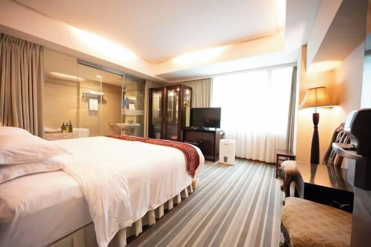 A hotel room with a large bed, a TV, a desk, and a chair.
