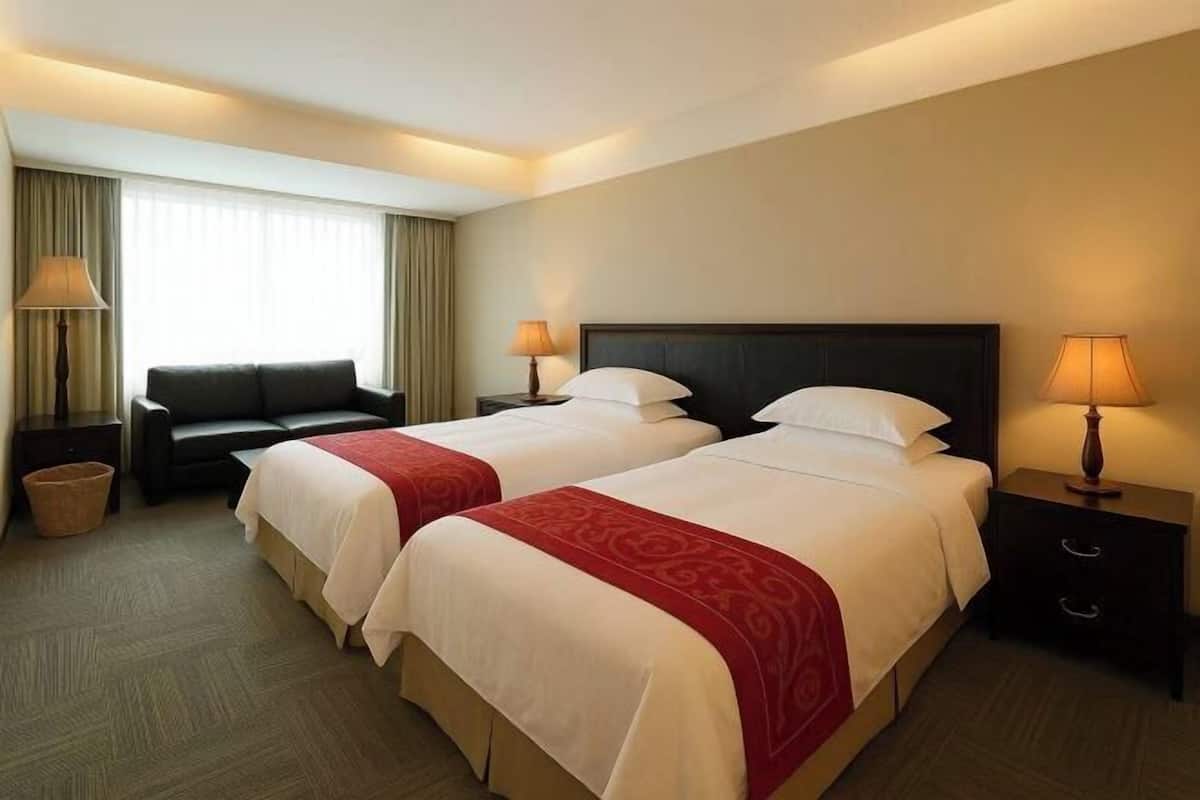 A hotel room with two beds, a sofa, a lamp, and a window with curtains.