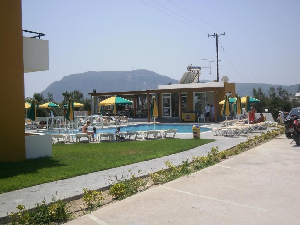 Un área de piscina con sillones de descanso y sombrillas, un edificio con ventanas amplias y una montaña al fondo.