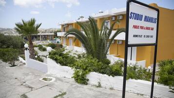 A yellow building with a sign for 'STUDIO MANOLIS' indicating a public pool and snack bar.