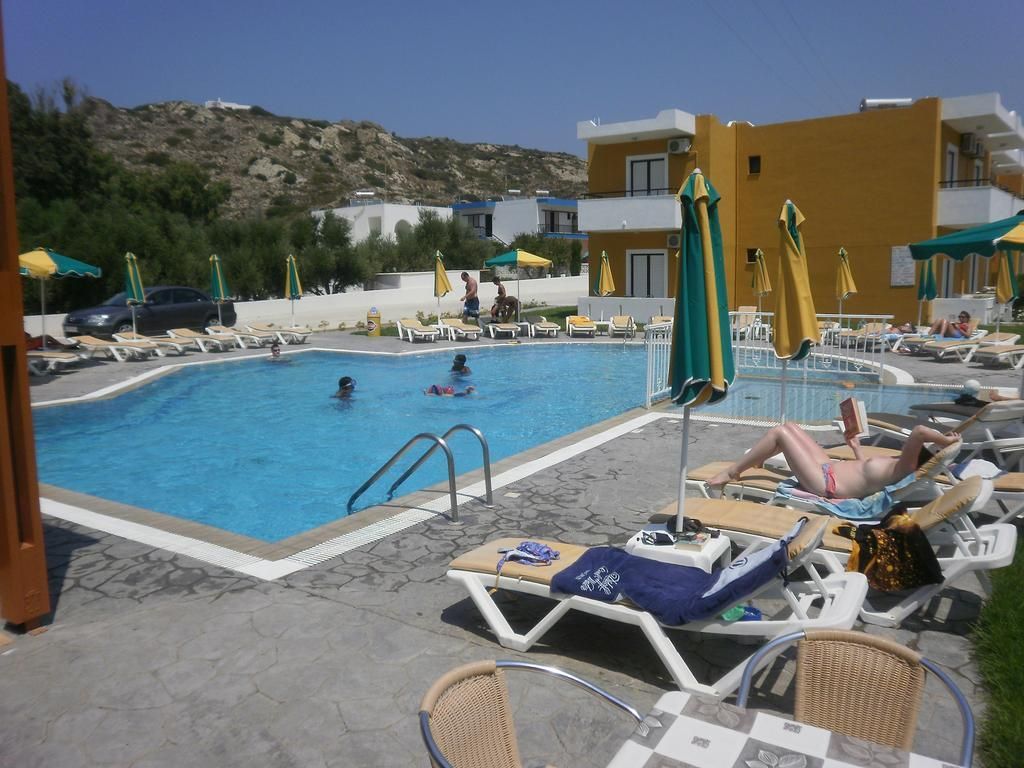 A poolside area with lounge chairs and umbrellas, a swimming pool, and a building in the background.