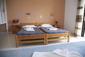A double bed with wooden frames and blue bedding, two bedside tables with lamps, and a window with curtains. - Manolis Studios (Kos)