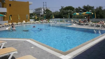Piscina com espreguiçadeiras e guarda-sóis, cercada por edifícios.