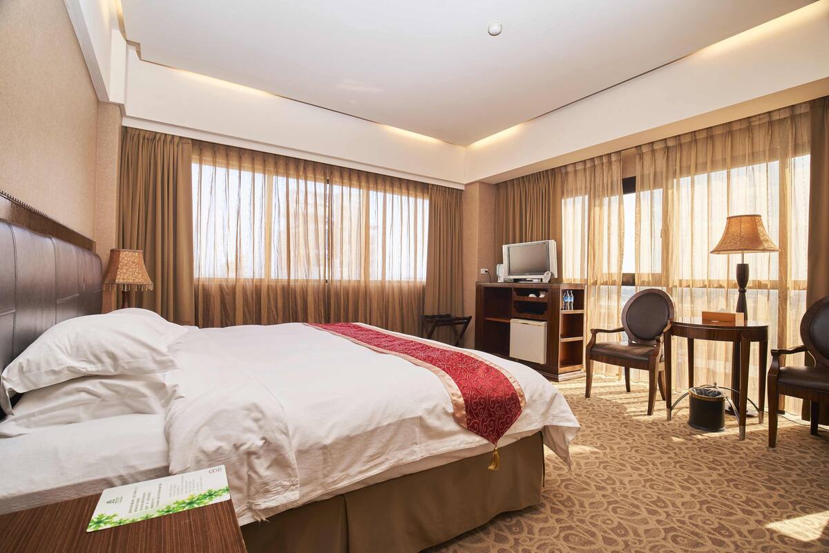 A hotel room with a large bed, a desk with a computer, a chair, and a lamp.