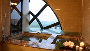 Un área de spa con un amplio ventanal arqueado, un jacuzzi y velas.