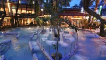 A pool area with a water feature, palm trees, and a building with illuminated windows.